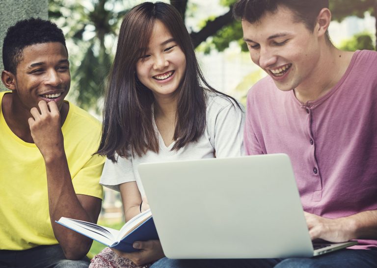 Three students working with a laptop and a textbook