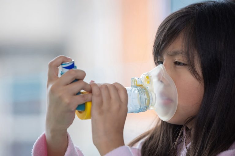 A young girl using an asthma inhaler mask